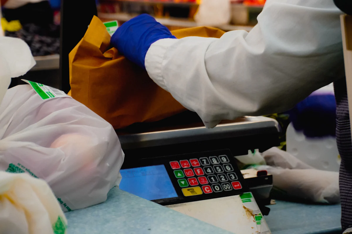 A cashier weighing loose groceries at a supermarket checkout