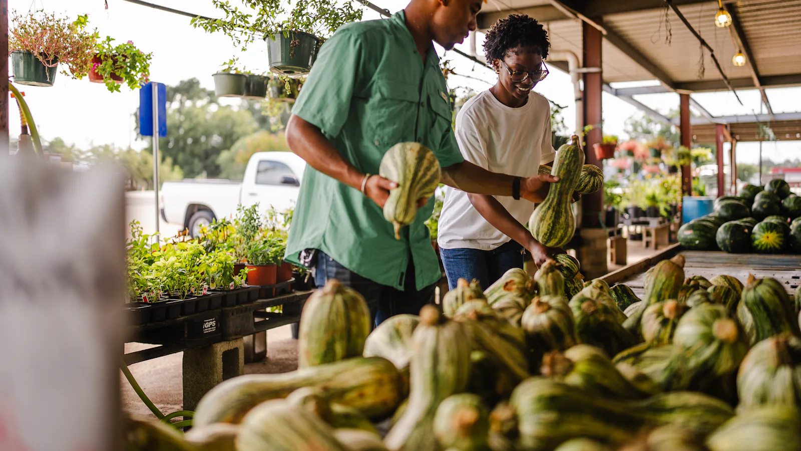 Two shoppers choosing squash and gourds at an outdoor produce market