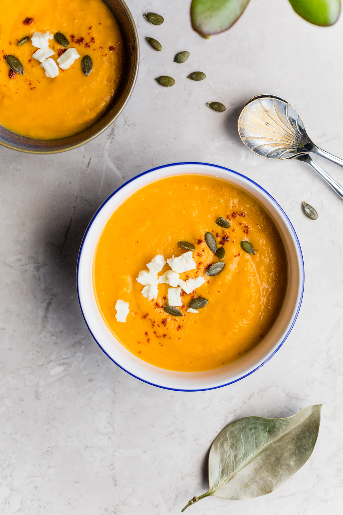 Bowls of orange soup topped with feta and pumpkin seeds