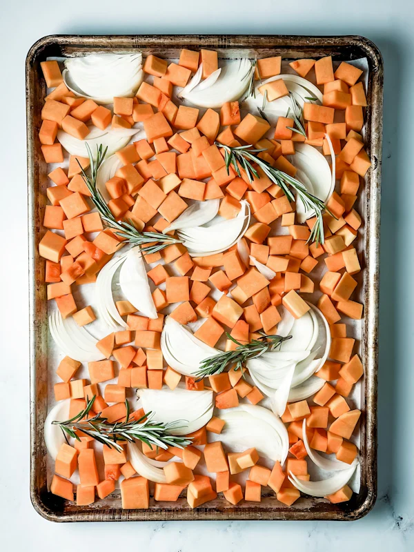 Diced sweet potatoes and onions with rosemary on a baking sheet